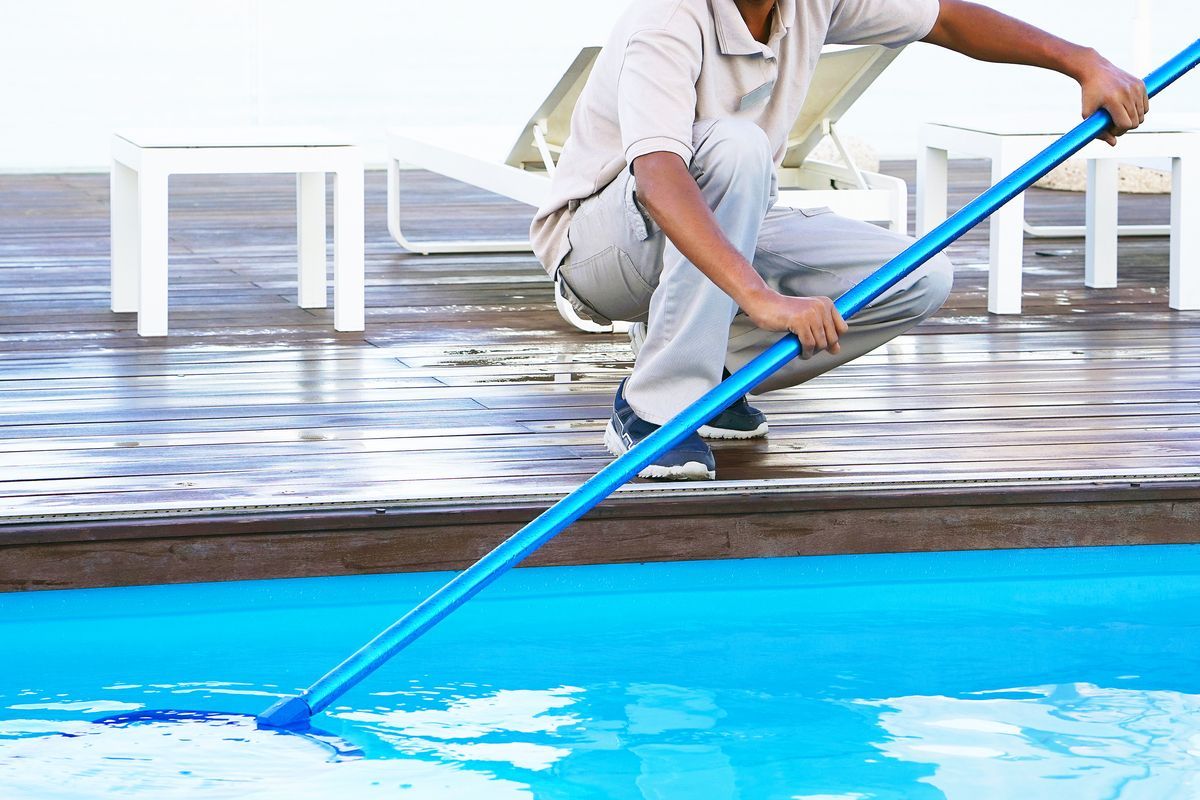 Hombre pasando el limpiafondos a la piscina para limpiarla