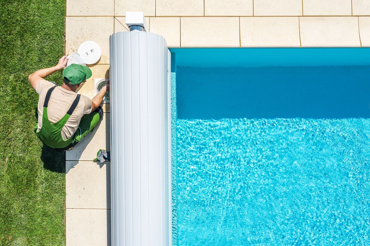 Hombre con mono verde arreglando desagüe de la piscina