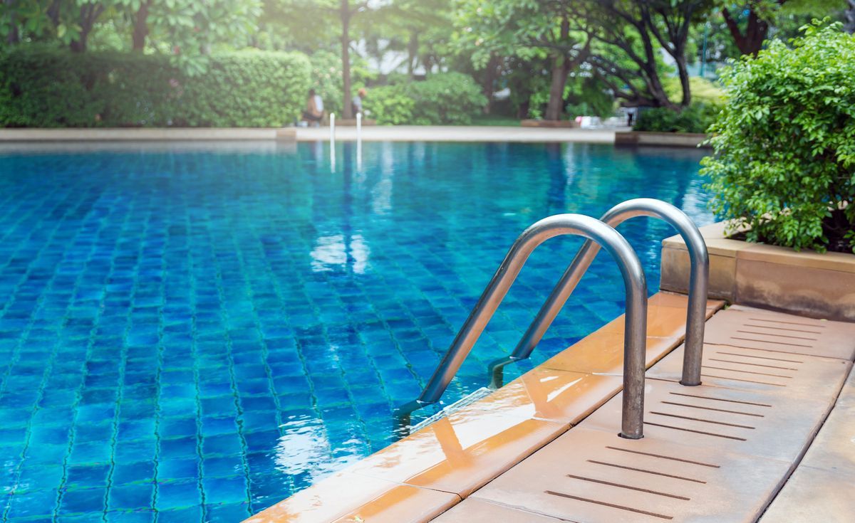 Piscina con fondo de cuadros azul, con escaleras y borde de madera rodeados de arboles