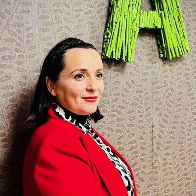 Una mujer con una chaqueta roja está parada frente a una letra h verde.