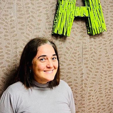 Una mujer sonríe delante de una letra a verde en una pared.