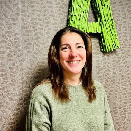 Una mujer con un suéter verde sonríe delante de una letra a verde.