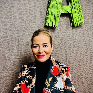 Una mujer con una chaqueta colorida sonríe delante de una letra a verde.