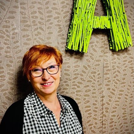 Una mujer con gafas sonríe delante de una letra a verde.