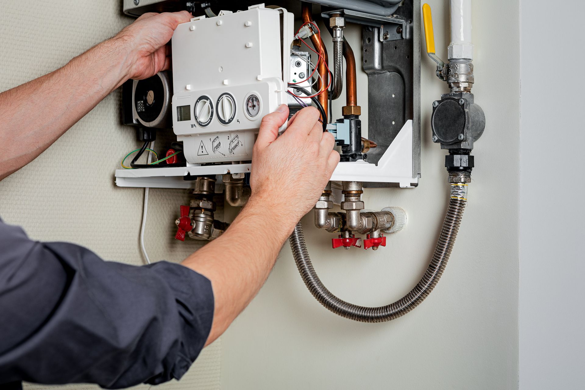 Un technicien effectue le réglage d'une chaudière à gaz ouverte avec des tuyaux et des câbles apparents à l'intérieur.