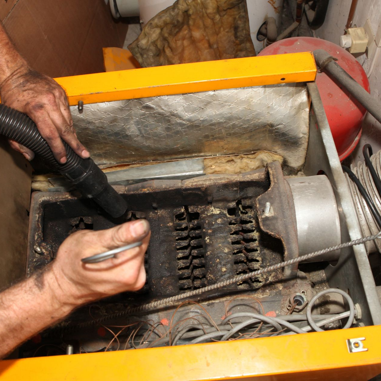 Des mains réparent l'intérieur ouvert d'une chaudière à fioul, outils et câblage visibles.