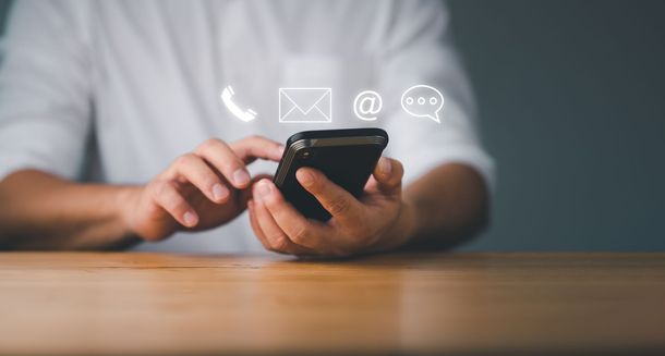 Des mains manipulant un smartphone sur une table, avec des icônes de contacts flottant au-dessus de l'écran.