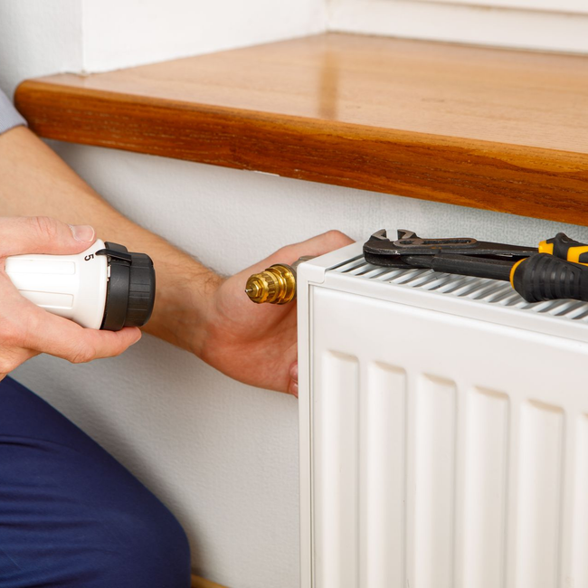 Une personne serre un robinet de radiateur avec une clé.