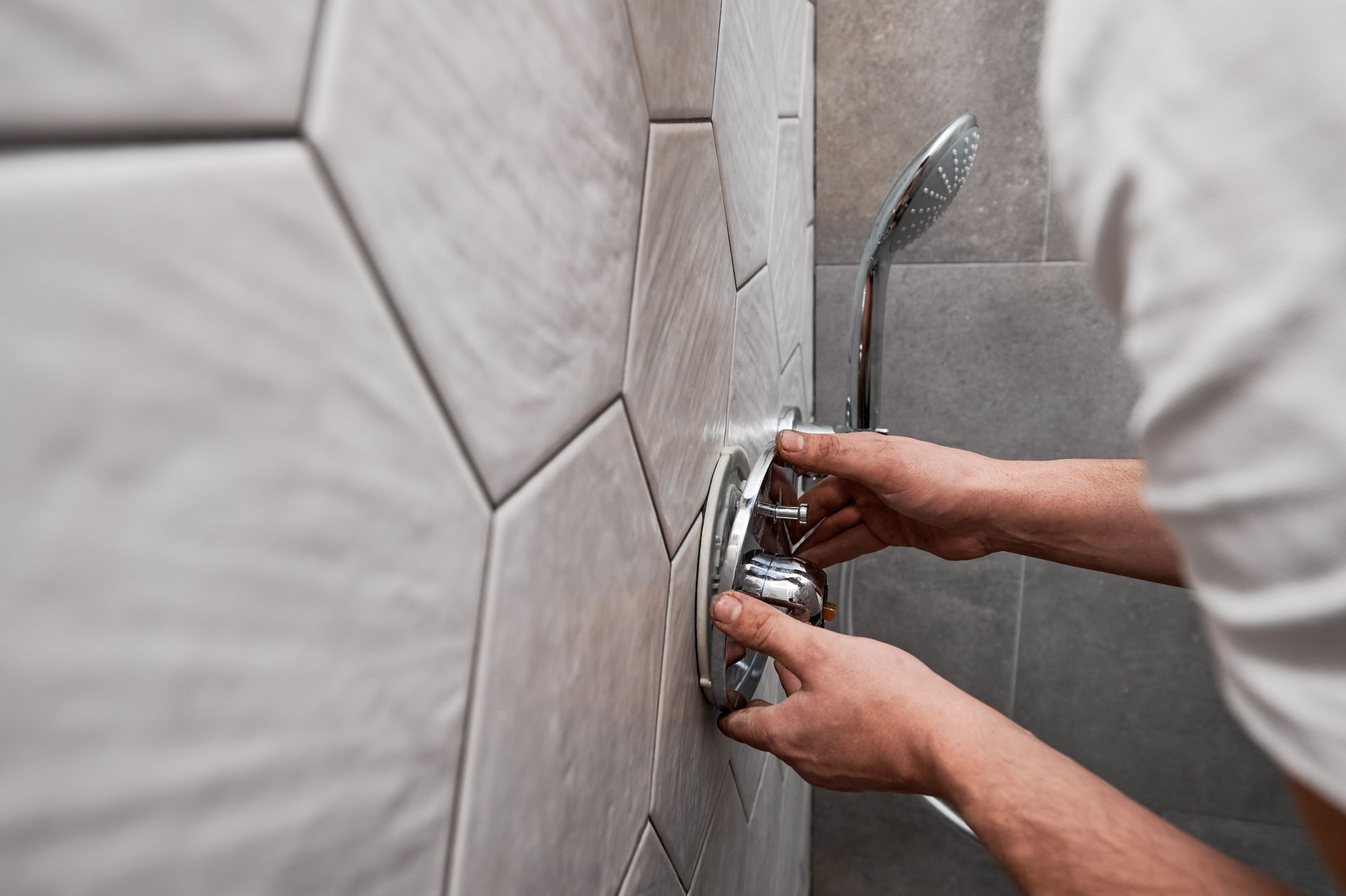 Mains installant un robinet de douche chromé sur un mur de salle de bains carrelé.