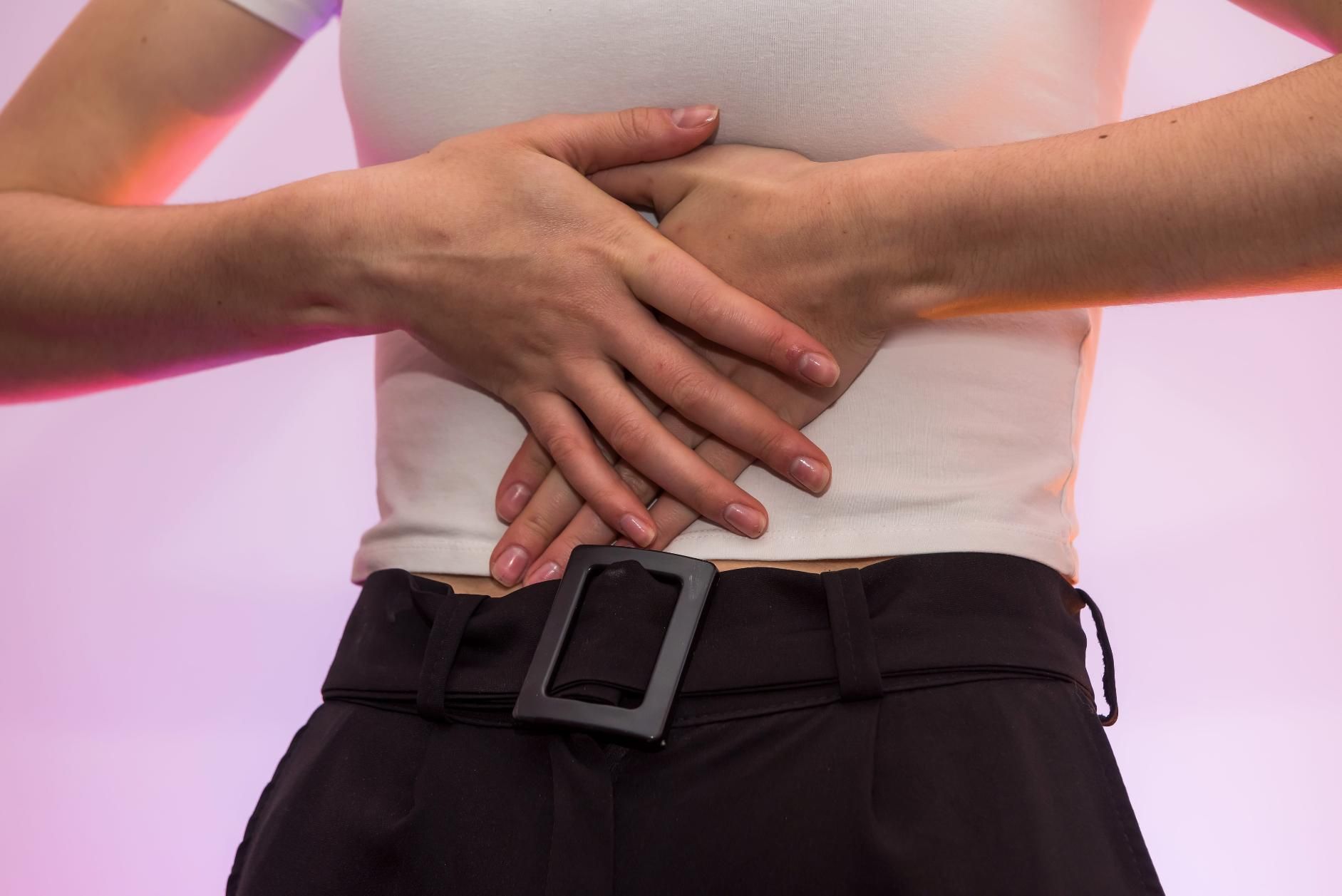 Con las manos entrelazadas sobre la parte baja de la espalda, vestía una blusa blanca y pantalones negros con cinturón.