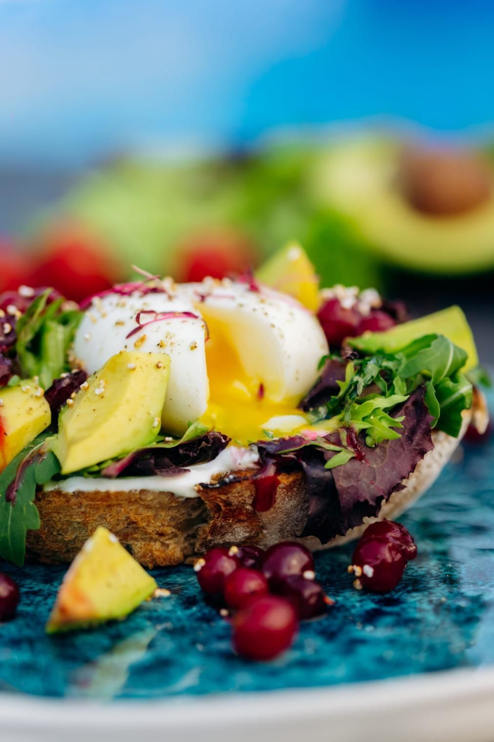 Tostada de aguacate con huevo escalfado y verduras, servida en un plato azul con frutos rojos.