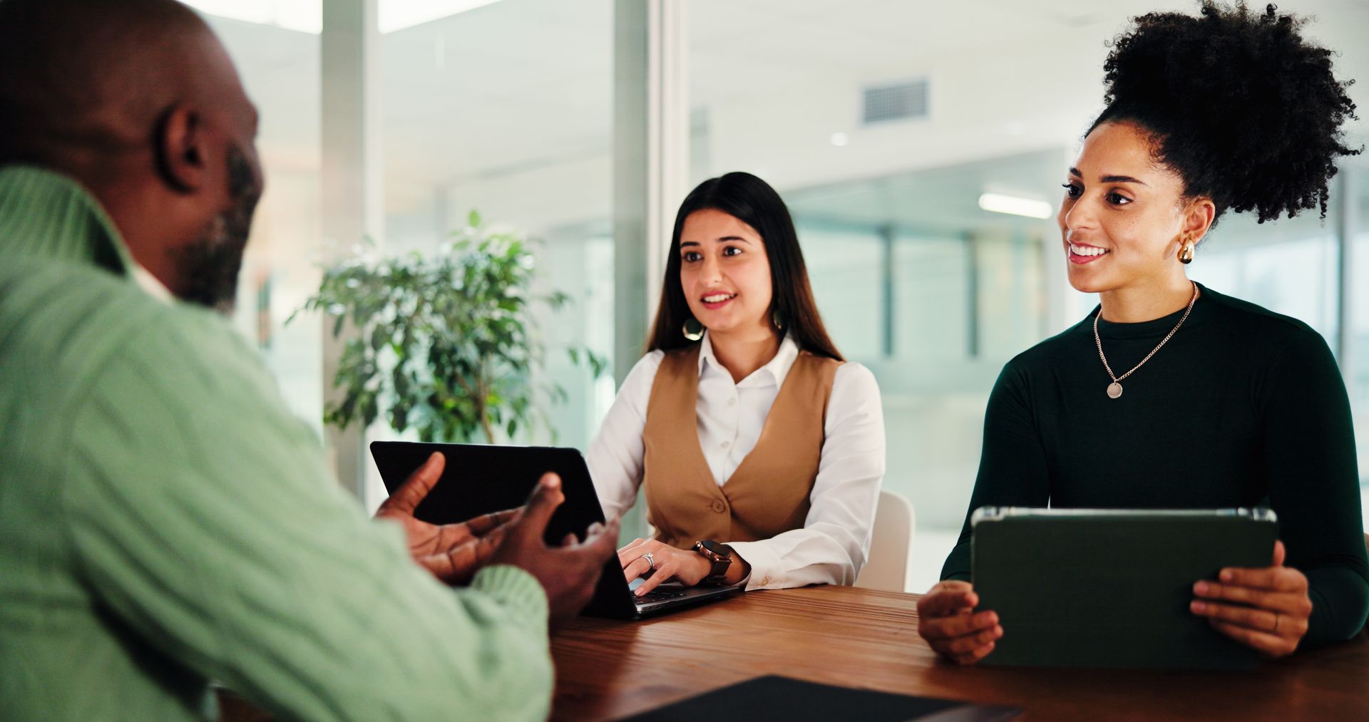 Trois collègues en réunion, assis à une table avec des tablettes dans un bureau lumineux.