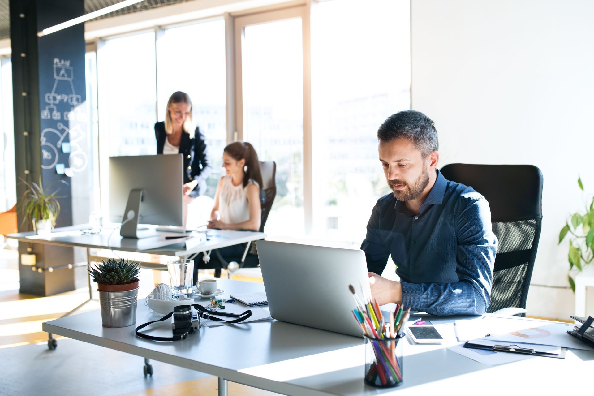 Des personnes travaillent dans un bureau moderne et lumineux, un homme utilisant un ordinateur portable à son bureau.