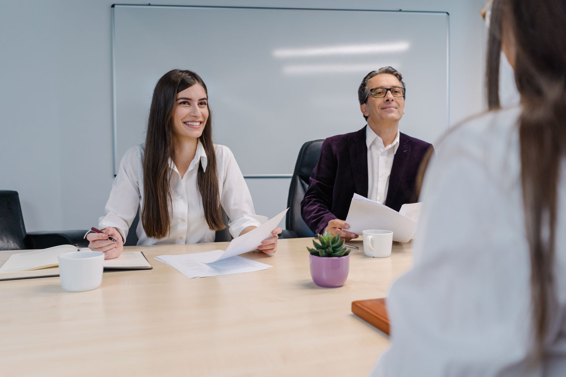 Entretien d'embauche dans une salle de conférence, avec deux personnes assises face à un recruteur.