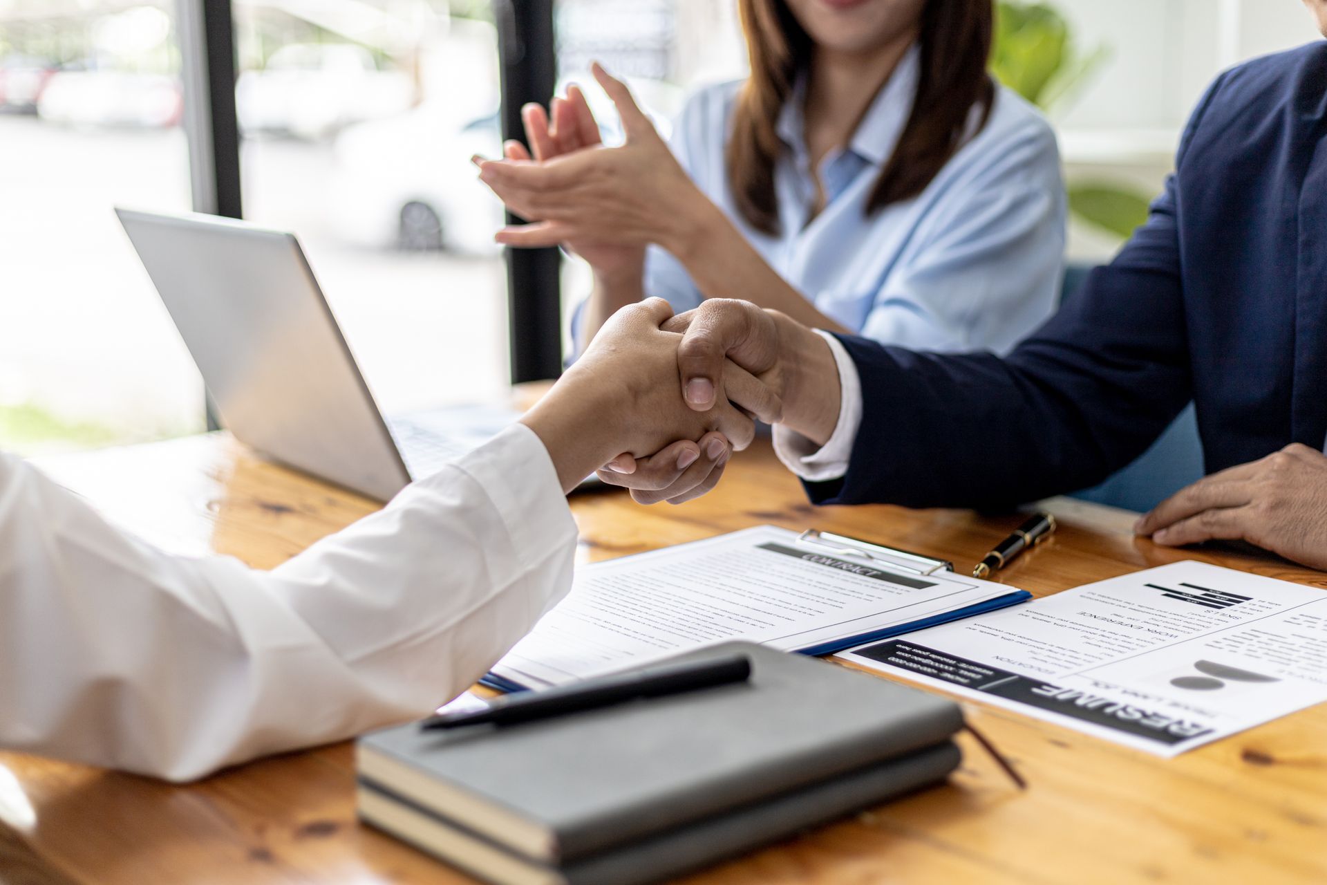 Réunion d'affaires, mains tremblantes, autour d'une table en bois, ordinateur portable, papiers et calculatrice à proximité.