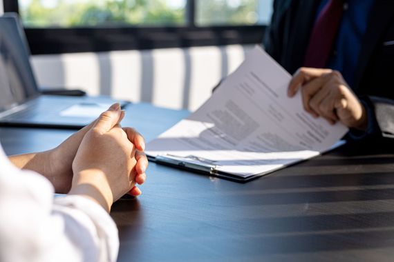 Deux personnes examinent des documents de part et d'autre d'une table de conférence.