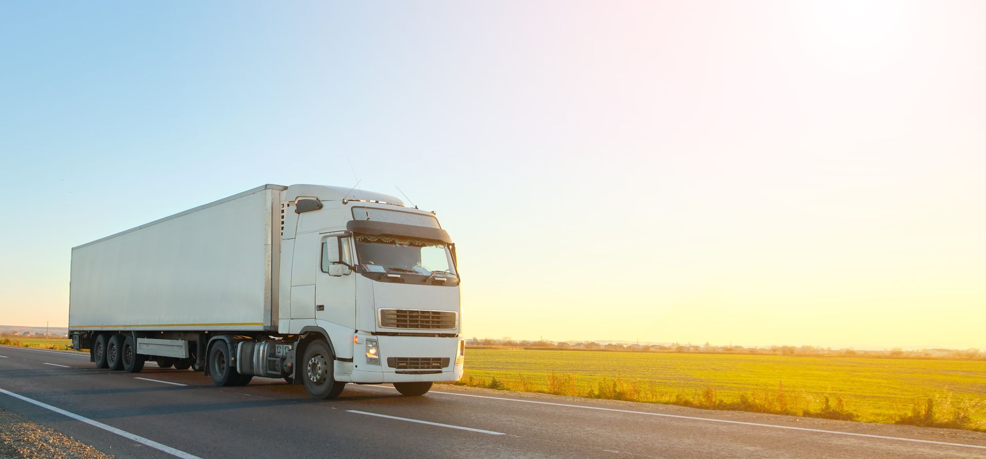 Un semi-remorque blanc roule sur une route de campagne.
