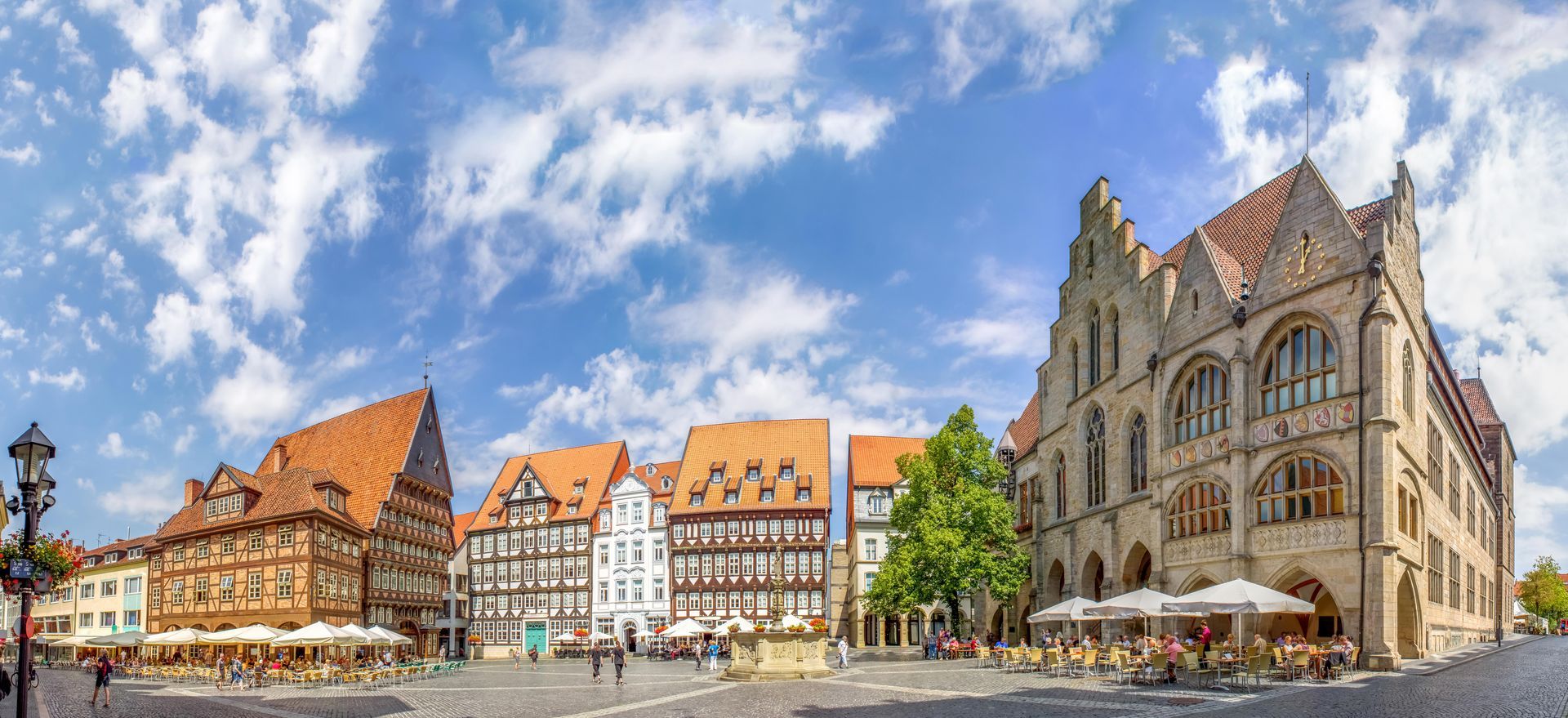 Ein Panoramablick auf einen Stadtplatz mit Gebäuden und Sonnenschirmen an einem sonnigen Tag.