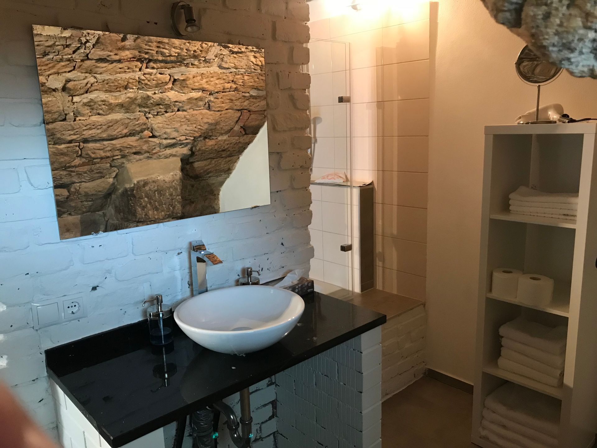 Badezimmer mit weißer Badewanne, Toilette und Waschtisch vor grauen Wänden, runder Spiegel.