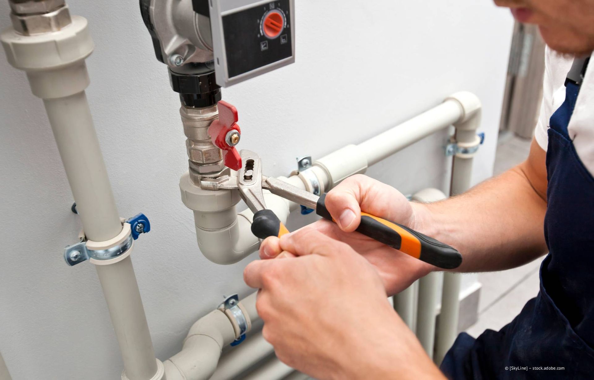 Ein Klempner arbeitet mit einer Zange an weißen Rohren mit einem roten Ventil in einem Hauswirtschaftsraum.