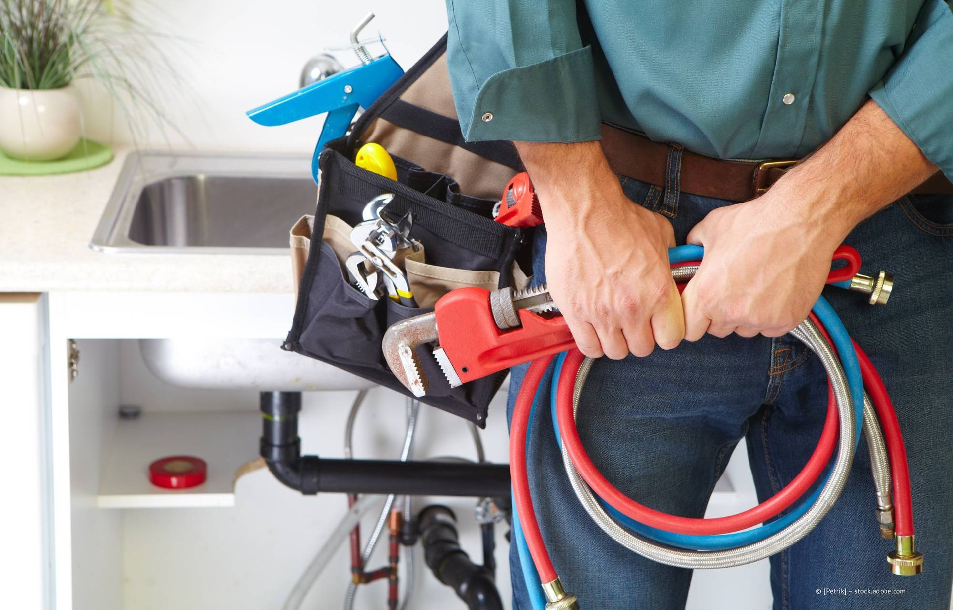 Ein Klempner hält Werkzeug und Schläuche in der Nähe einer Küchenspüle.