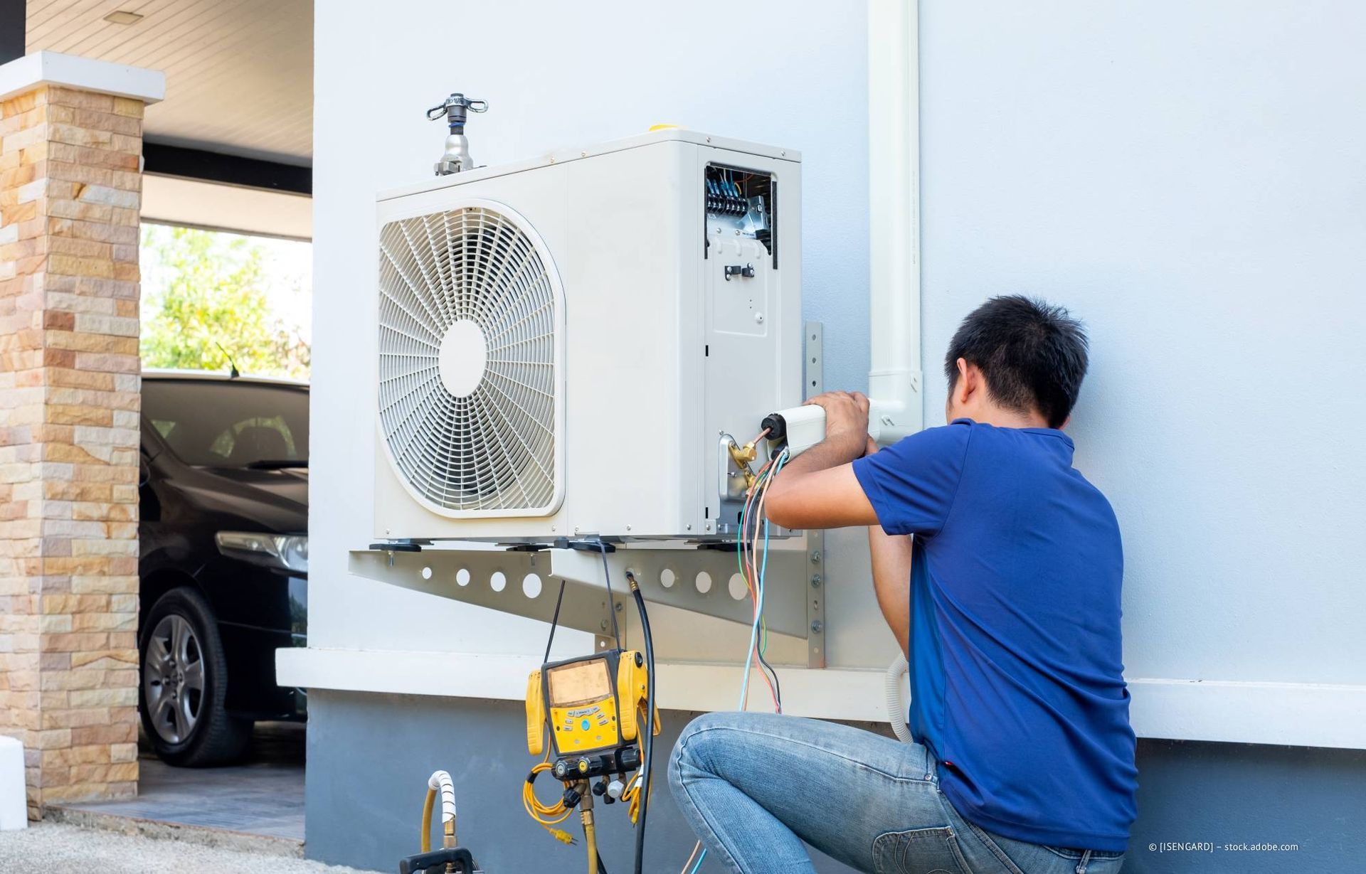 Ein Mann installiert eine Klimaanlage im Außenbereich eines Hauses. Er arbeitet an der Seite des weißen, an der Wand montierten Geräts.