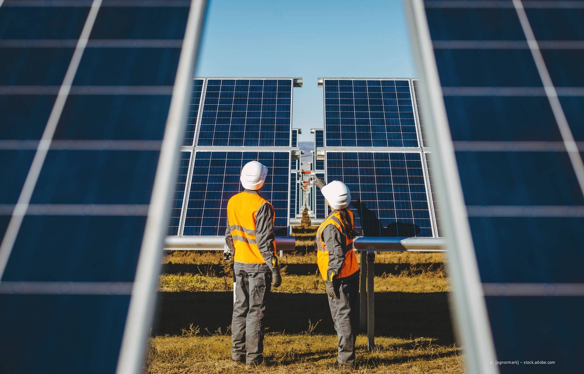 Arbeiter in Sicherheitswesten und Schutzhelmen inspizieren an einem sonnigen Tag Solarpaneele.