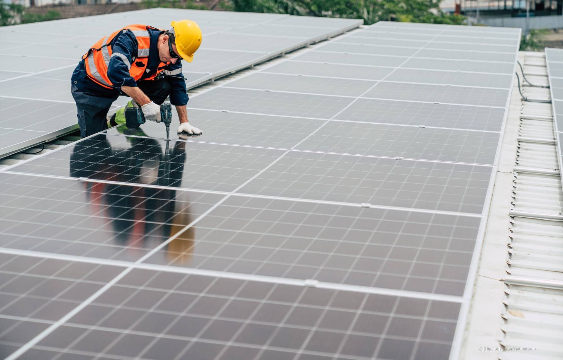 Ein Arbeiter in Schutzausrüstung installiert Solarpaneele auf einem Dach.