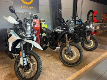 Tres motocicletas de aventura expuestas en una sala de exhibición, incluyendo una moto blanca en primer plano y motos negras detrás.