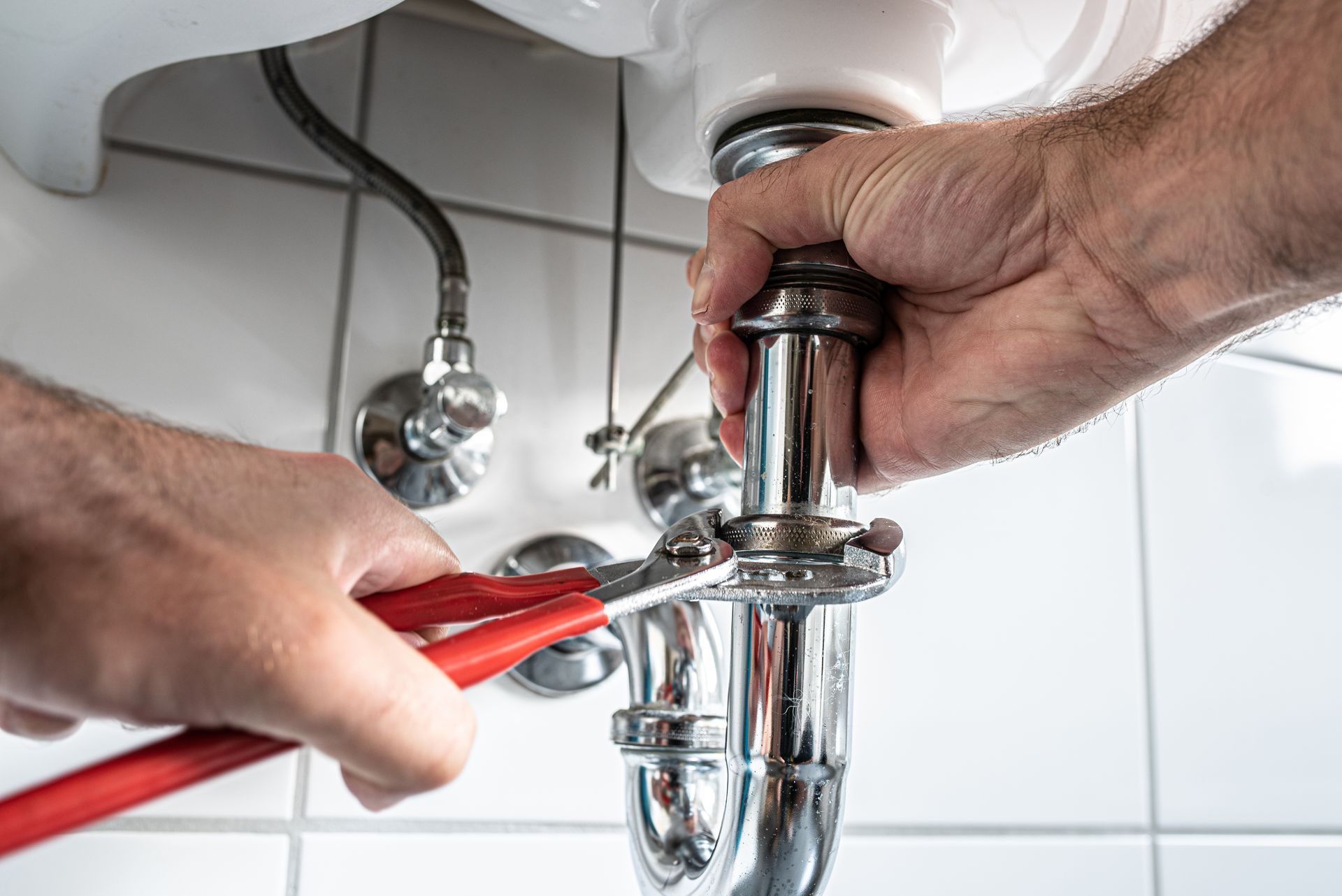 Homme réparant un siphon d’évier avec une clé à molette dans une salle de bains
