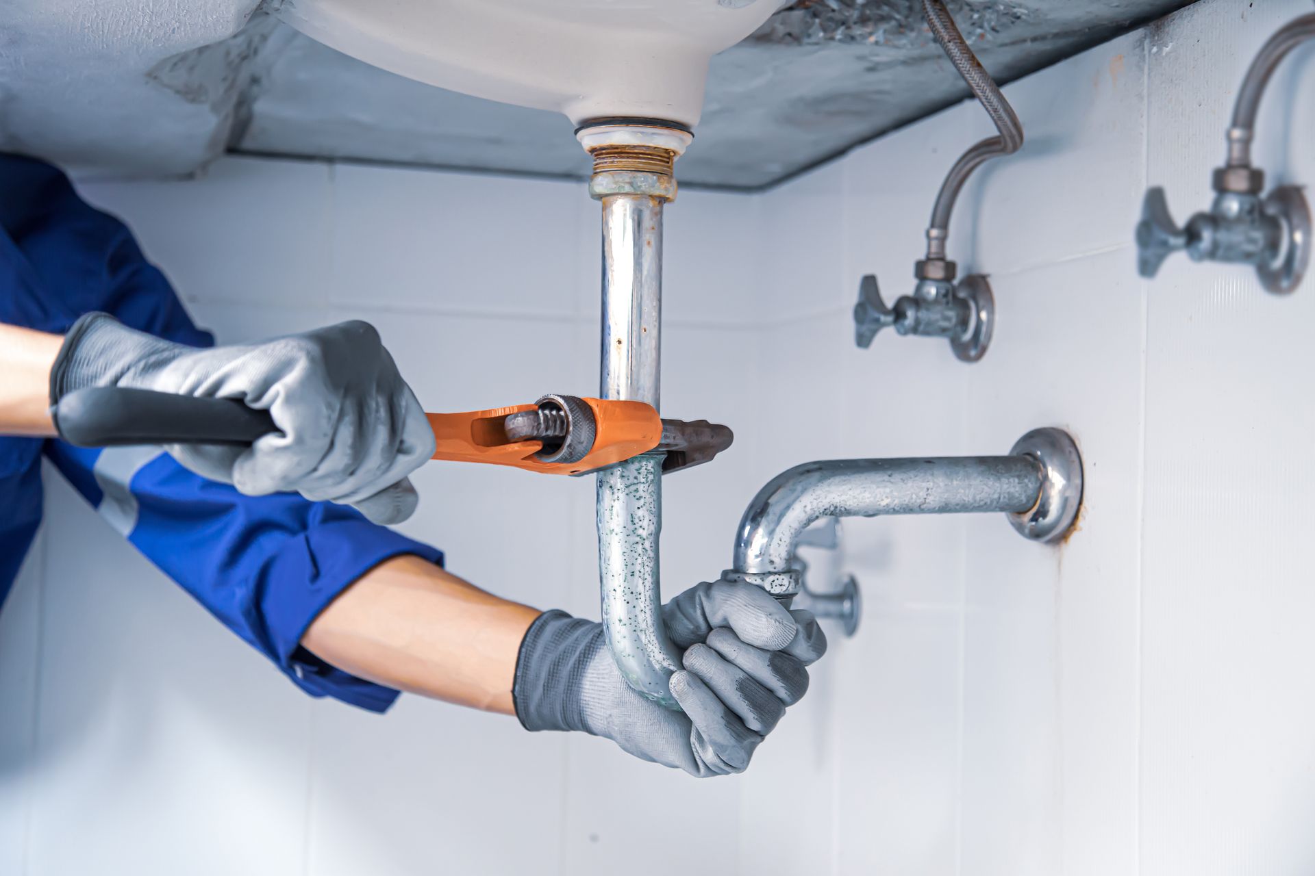 Personne en train de réparer un siphon d’évier avec une clé à molette sous un lavabo