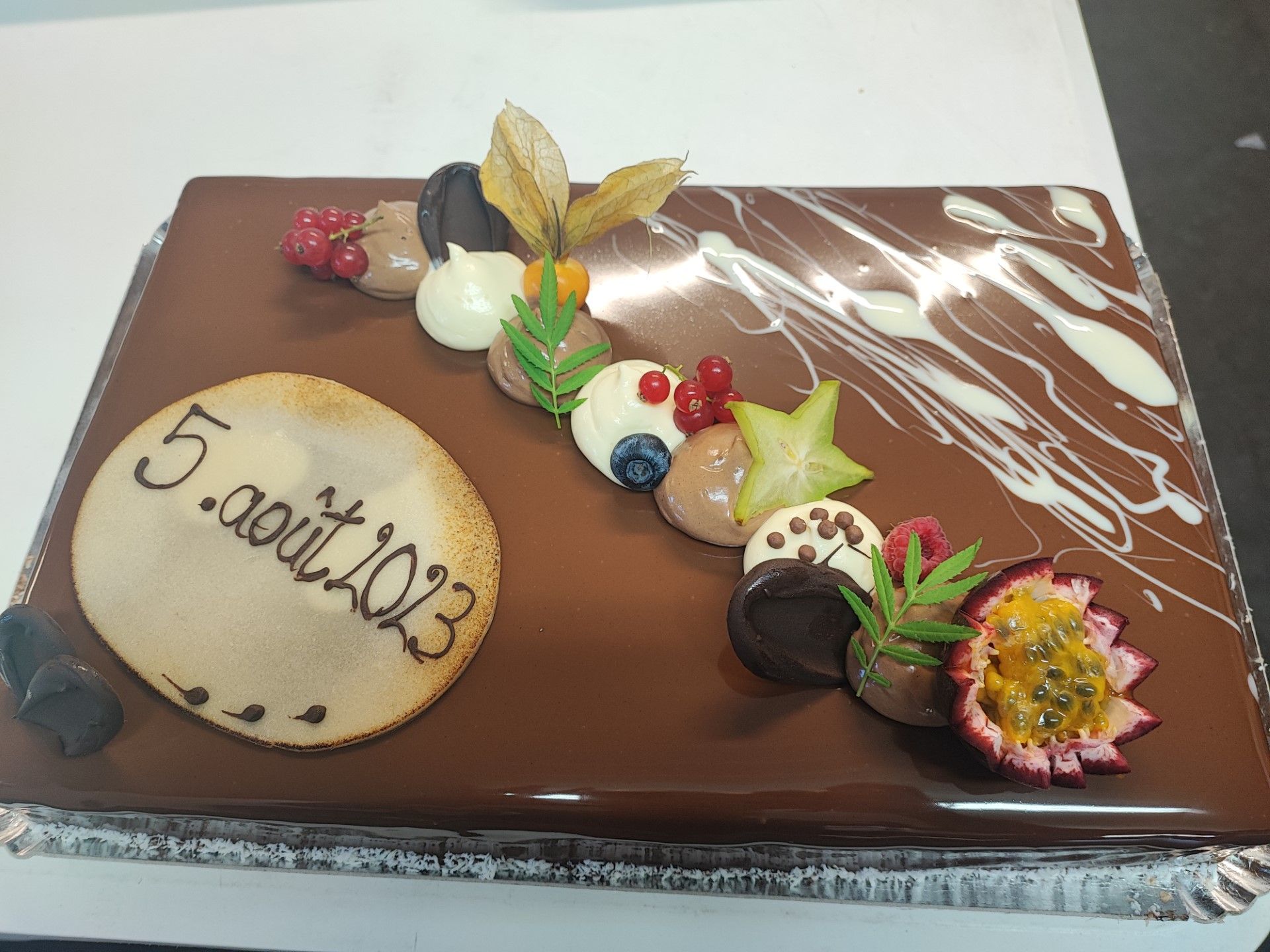 Gâteau avec un glaçage au chocolat avec quelques décorations et un rond mentionnant la date du 5 août 2023