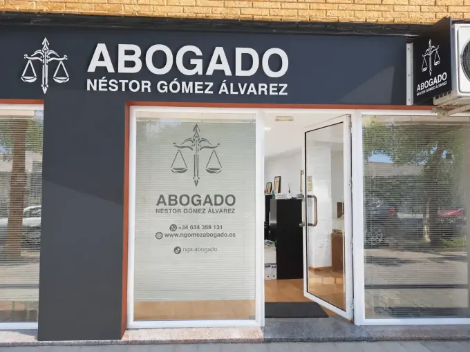 Fachada de un bufete de abogados con letrero “ABOGADO NÉSTOR GÓMEZ ÁLVAREZ” y puerta de cristal.