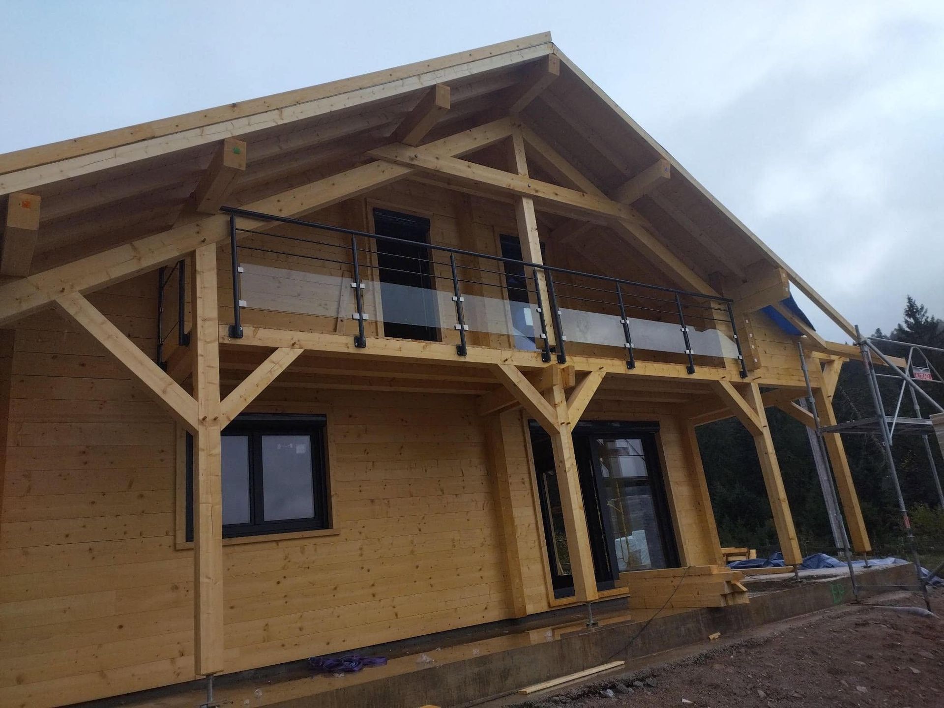 Façade d'une maison en bois avec un balcon qui possède des garde-corps en verre.