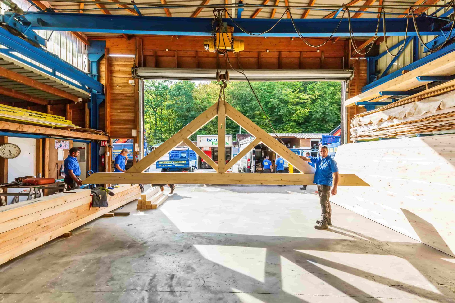 Une charpente en bois est soulevée à l'intérieur d'un atelier.