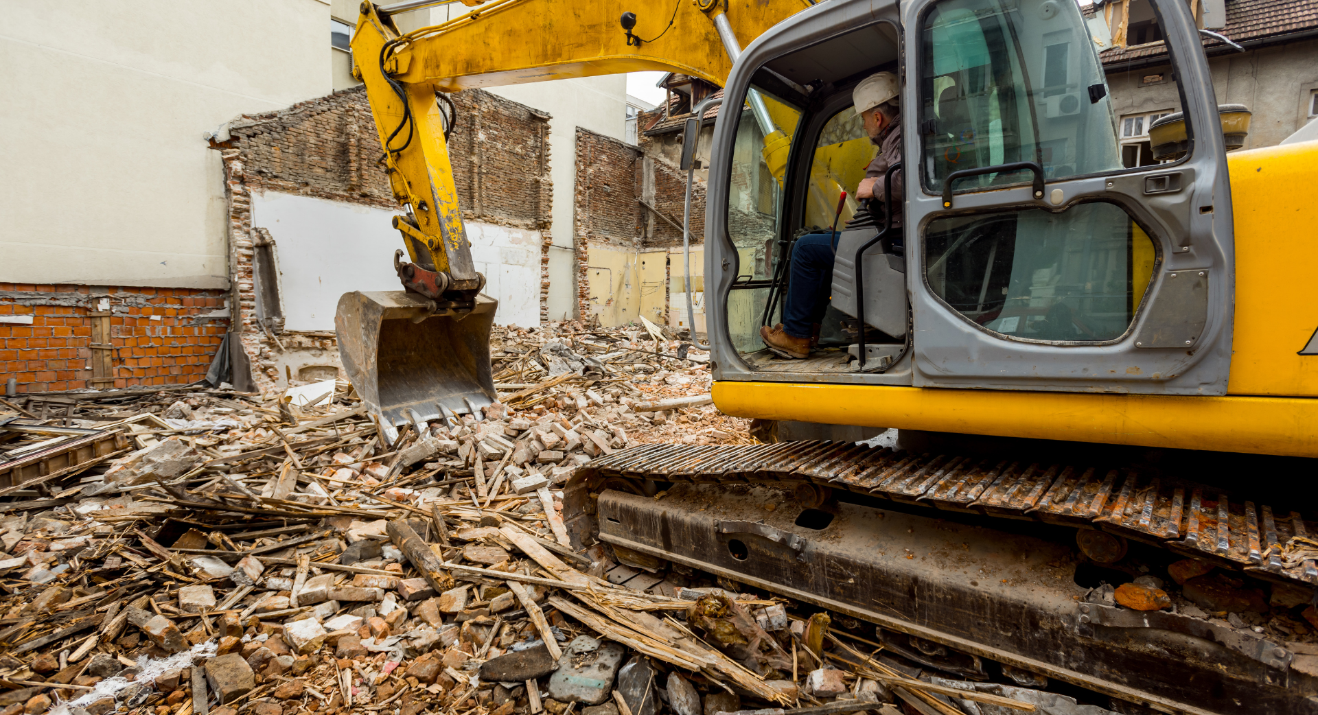Excavatrice jaune démolissant un bâtiment, décombres et débris au premier plan.