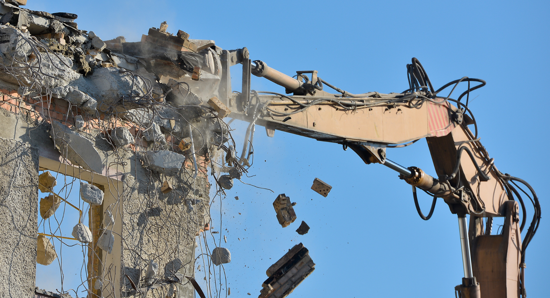 Excavatrice jaune démolissant un bâtiment, débris éparpillés tout autour ; journée nuageuse.