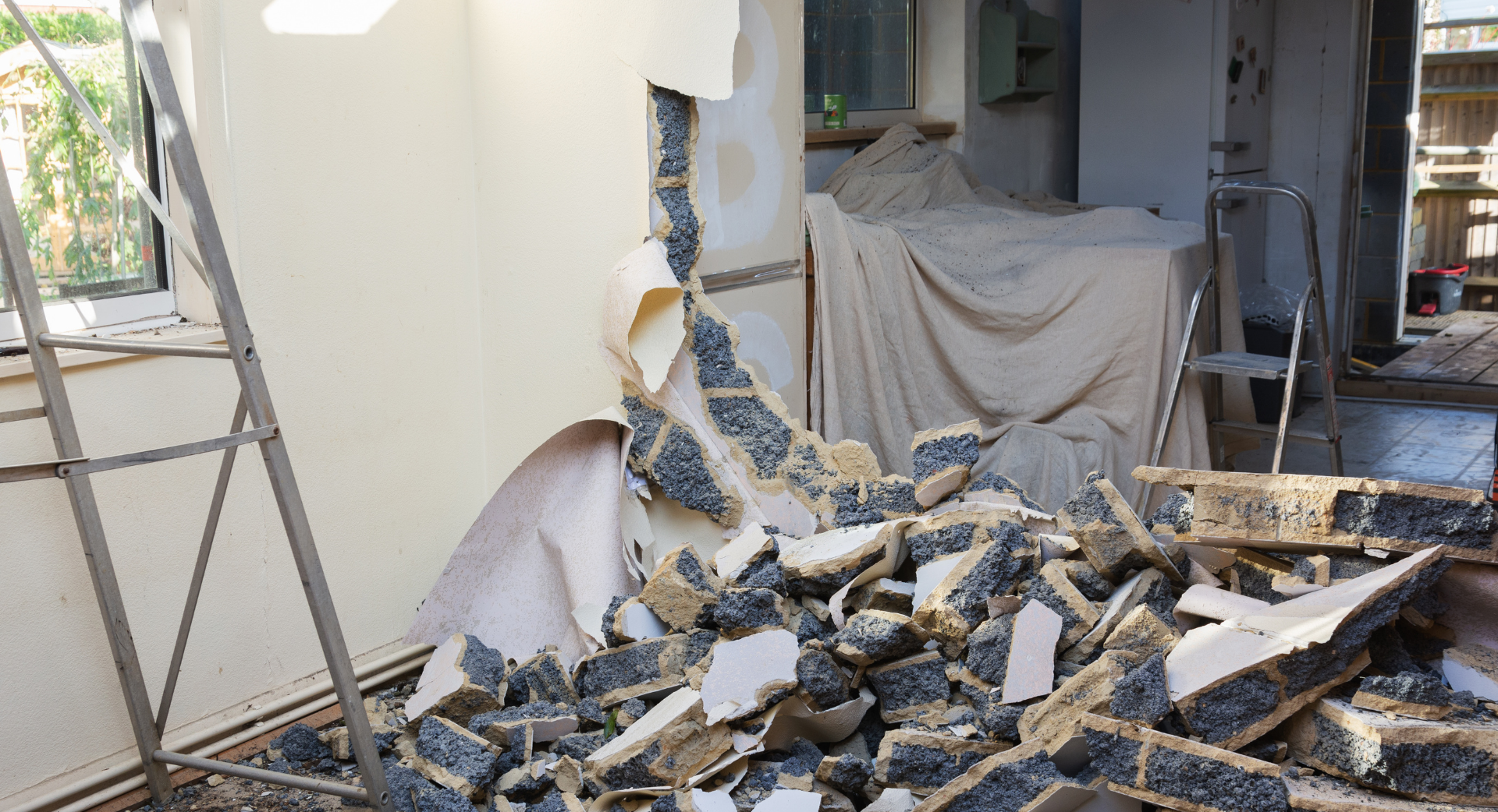 Excavatrice jaune démolissant un bâtiment, décombres et débris au premier plan.