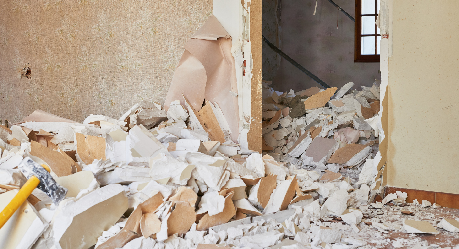 Excavatrice jaune démolissant un bâtiment, débris éparpillés tout autour ; journée nuageuse.