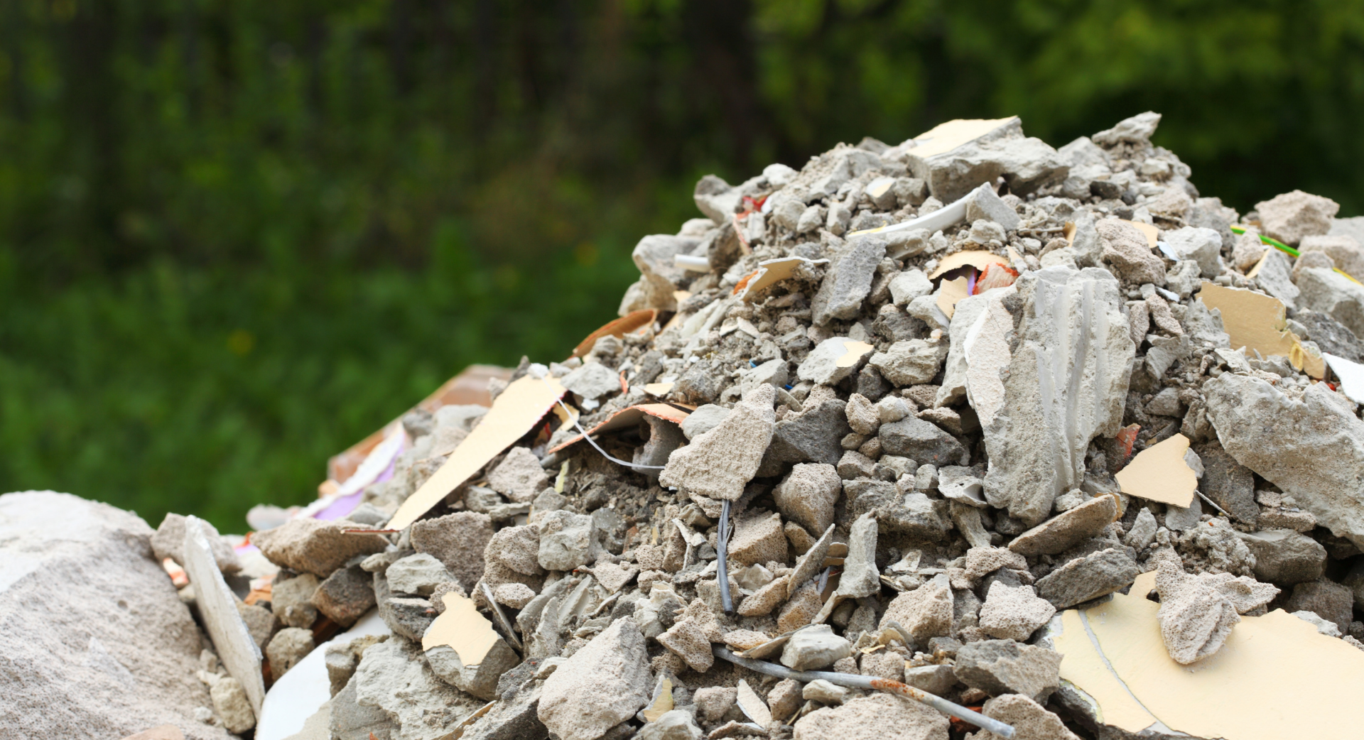Tas de débris de construction : béton brisé, bois et gravats, à l'extérieur, sur fond vert.