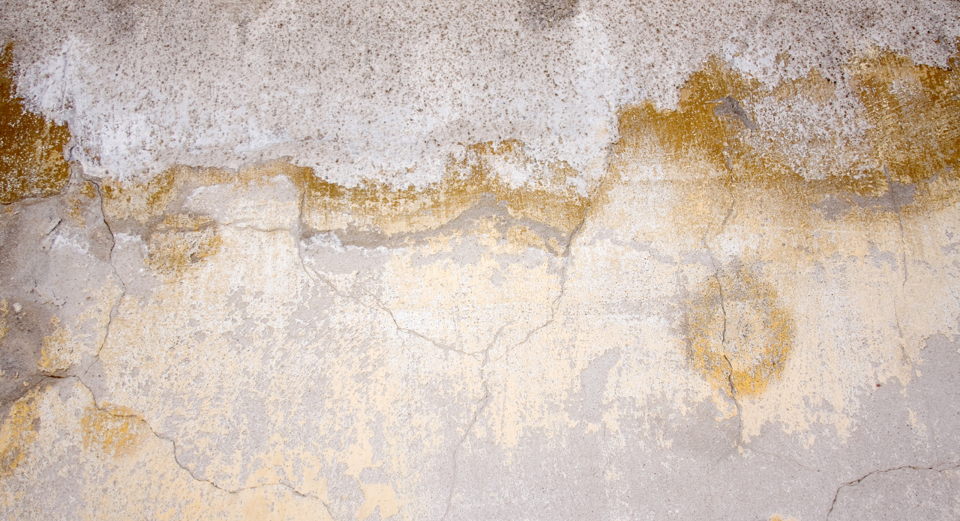 Mur de béton fissuré et taché avec décoloration jaune et grise.