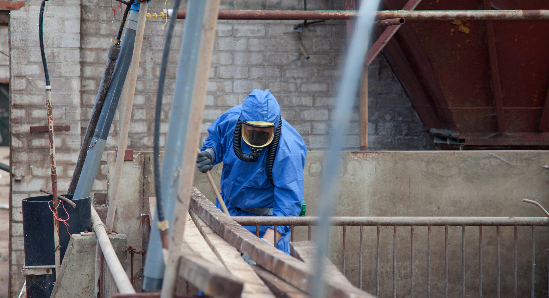 Une personne en combinaison bleue de protection contre les matières dangereuses sur une structure métallique.
