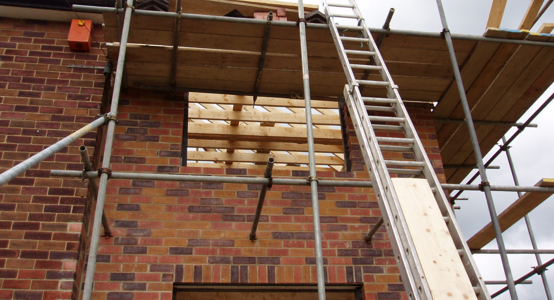 Des ouvriers construisent un mur en parpaings à l'extérieur. L'un mesure, l'autre tient un bloc.