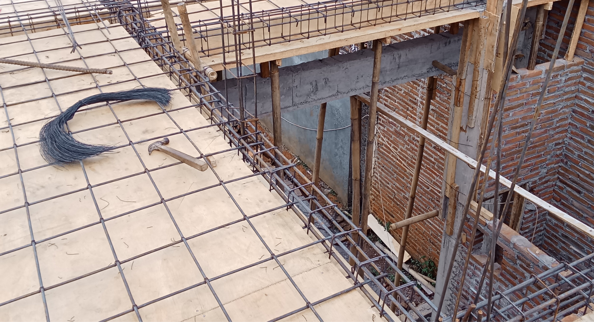 Chantier de construction avec ossature en fer pour dalle béton. Supports et murs en bois, treillis métallique et marteau visibles.