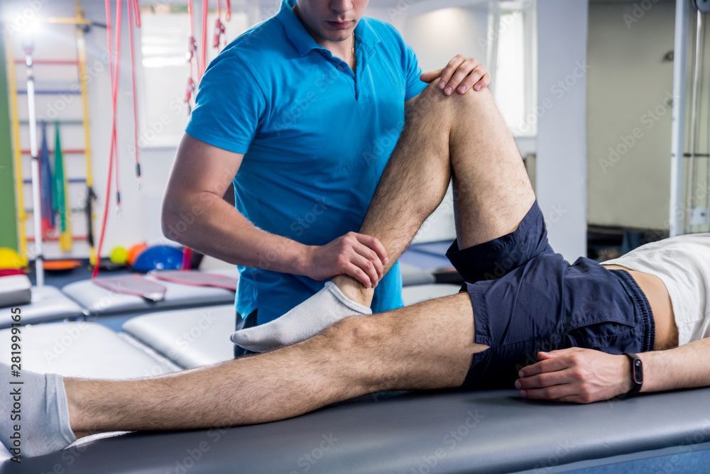 Physiotherapeut dehnt das Bein eines Patienten auf einer Behandlungsliege in einer Klinik