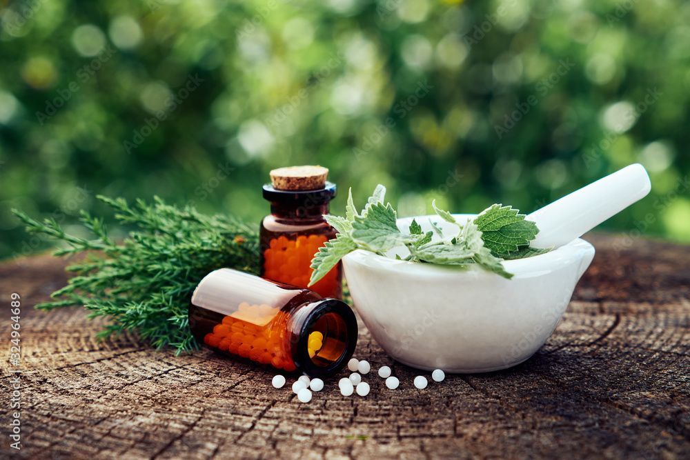 Kräutermörser und Stössel mit frischen grünen Blättern, bernsteinfarbenen Flaschen und weissen Perlen auf einer rustikalen Holzoberfläche
