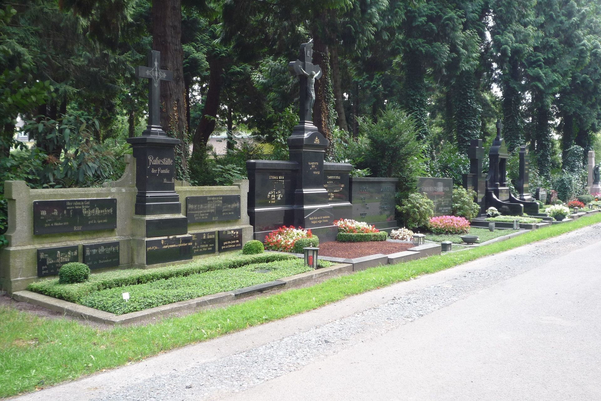 Reihen schwarzer Gedenkgrabsteine ​​mit Blumen säumen eine von Bäumen gesäumte Friedhofsstraße