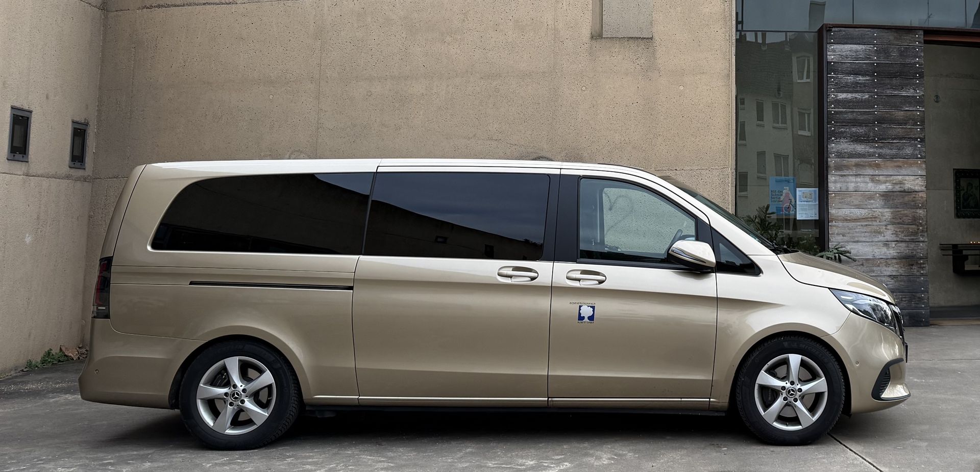 Beiger Minivan parkt neben einem Gebäude, Seitenansicht.