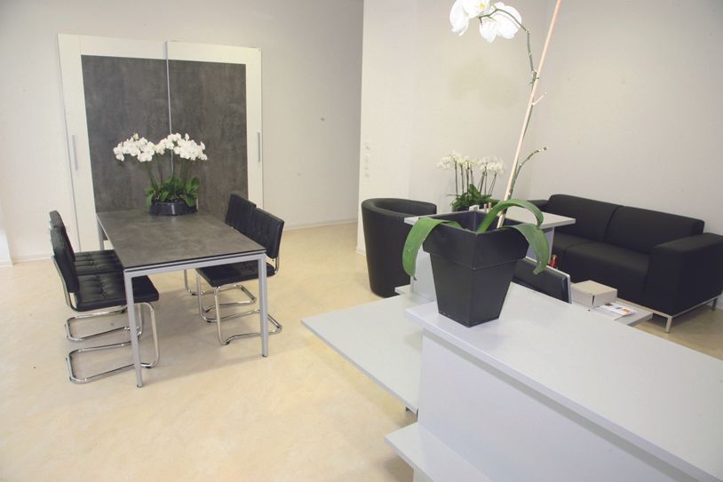Moderner Wohn- und Essbereich mit schwarzen Möbeln, grauem Tisch und weißer Orchideendekoration