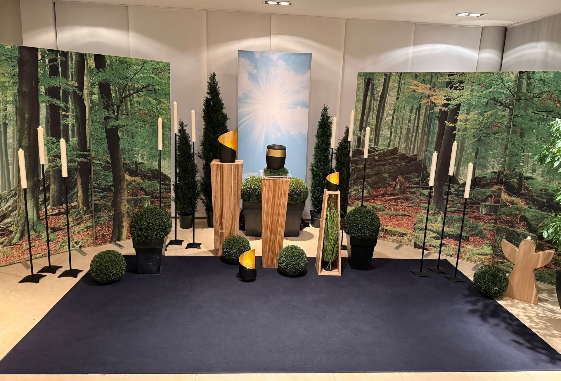 Innenbereich mit Waldmotiv: Bäume, Grünpflanzen und Baumstümpfe auf dunkelblauem Boden vor Wandmalereien.